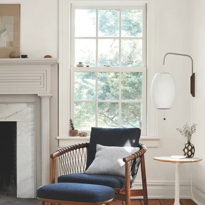 A cozy living room scene featuring a mid-century modern armchair with a matching ottoman, a white wall sconce, and a fireplace in the background.