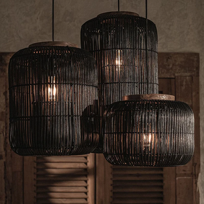 Three black rattan lantern pendant lights hanging at different heights against a dark curtain backdrop.
