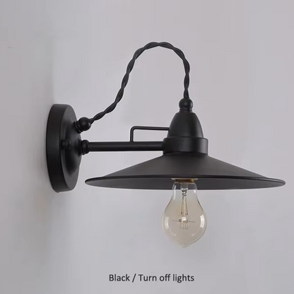 A black metal swing-arm wall sconce with a wide conical shade and a twisted corded arm, shown mounted on a light gray wall. An Edison-style bulb is visible inside, and the text 'Black / Turn off lights' appears at the bottom.