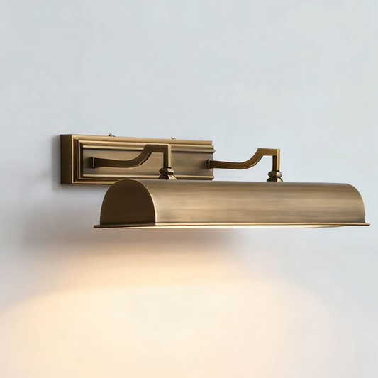 An adjustable wall-mounted reading light fixture in a brushed antique brass finish, shown illuminated against a plain light gray wall.