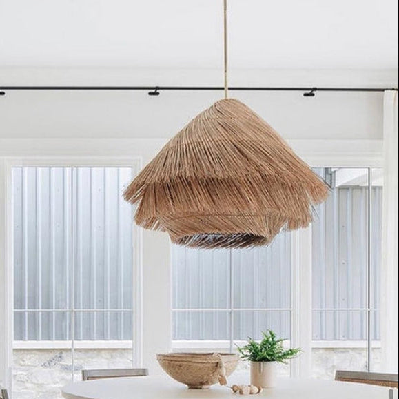 Shaggy straw dome hanging lamp with tiered fringe natural fibers and a brass ceiling mount.