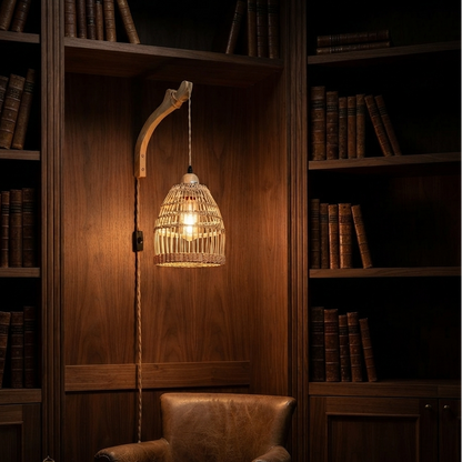 A warm, glowing pendant lamp with a woven rattan shade hangs in a dark wood library nook beside a brown leather armchair and bookshelves.