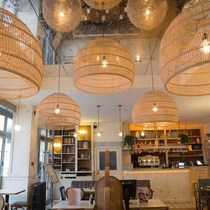  Large rattan pendant lights hanging from a mirrored ceiling in a modern restaurant interior with wooden furniture.