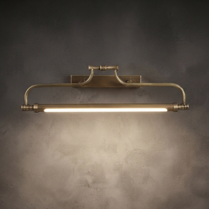 A vintage-style industrial wall sconce with a brushed brass finish, featuring a horizontal bar with a glowing light tube, mounted on a textured dark gray wall.