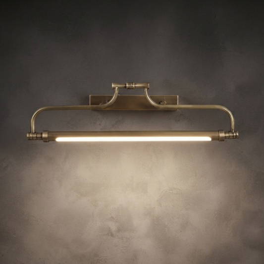 A vintage-style industrial wall sconce with a brushed brass finish, featuring a horizontal bar with a glowing light tube, mounted on a textured dark gray wall.