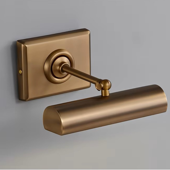 A modern wall-mounted light fixture with a cylindrical shade and rectangular backplate in a brushed brass or bronze finish, shown against a plain gray wall.