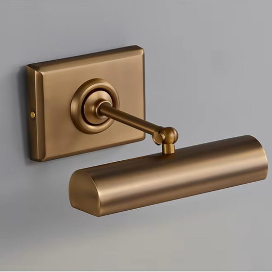 A modern wall-mounted light fixture with a cylindrical shade and rectangular backplate in a brushed brass or bronze finish, shown against a plain gray wall.