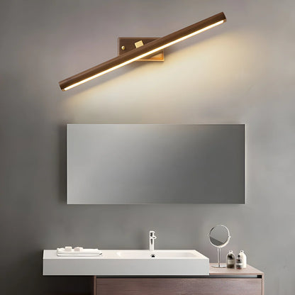 A modern wall-mounted light fixture with a long cylindrical shade and warm illuminated LED strip, shown above a bathroom mirror and sink in a real interior setting.
