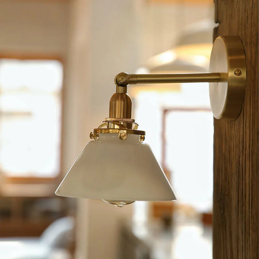 Wall-mounted lamp with white shade and gold fixture in a blurred indoor setting