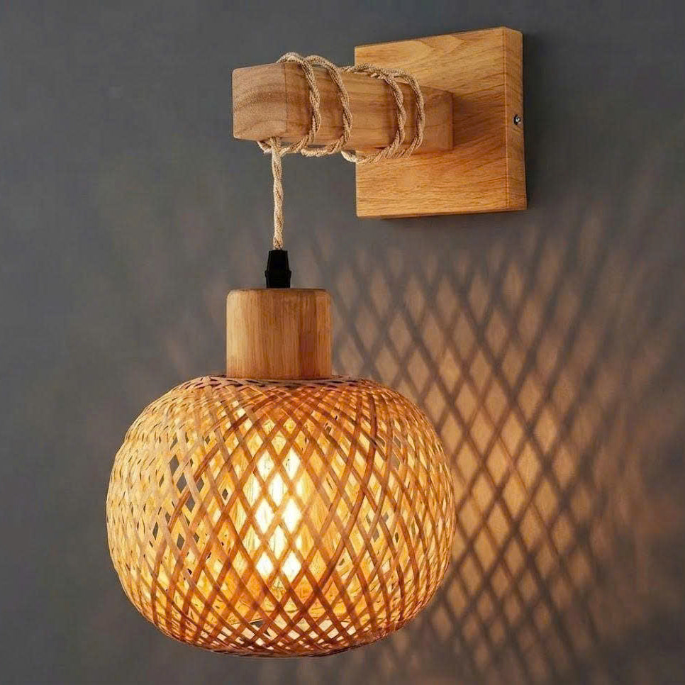 A warm-toned wall-mounted pendant light with a woven rattan globe shade, a natural wood ceiling mount, and a visible cast shadow on the gray wall behind it.