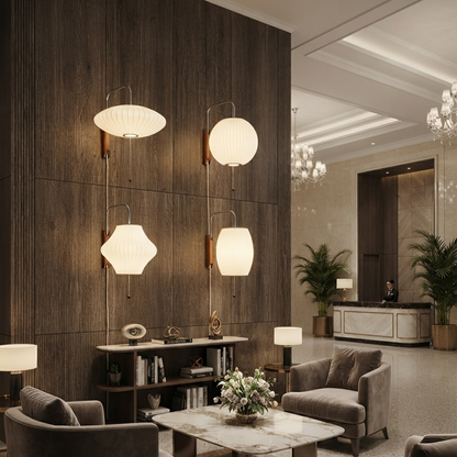 A modern interior lobby with dark wood paneling, four wall-mounted pendant lights with white ribbed shades, upholstered armchairs, a marble-top coffee table, and a reception desk in the background.