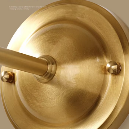 Close-up of a brushed brass or gold metal wall fixture base with a mounting rod and two visible screws on a warm beige background.