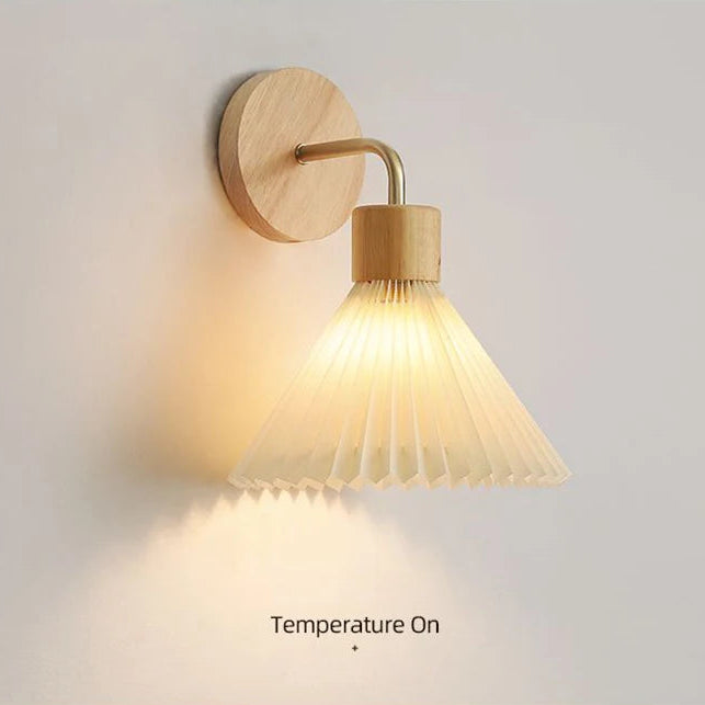 Wall-mounted light fixture with wooden finish and pleated design on a neutral background