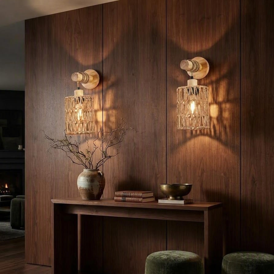Two matching wall sconces with warm glowing bulbs and textured cylindrical shades, mounted on a dark wood-paneled wall above a console table in a styled interior setting.