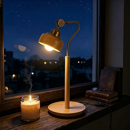 A warm-toned adjustable table lamp with a round wooden base and curved neck stands on a windowsill at night, glowing beside a lit candle and stacked books. The window shows a starry blue evening sky outside.