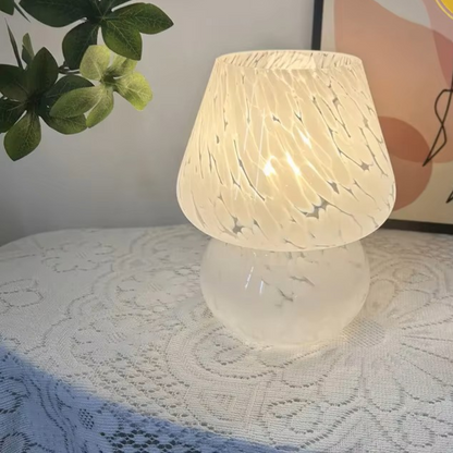 A glowing table lamp with a textured, crackled white shade and a frosted white base, placed on a white lace-covered surface.
