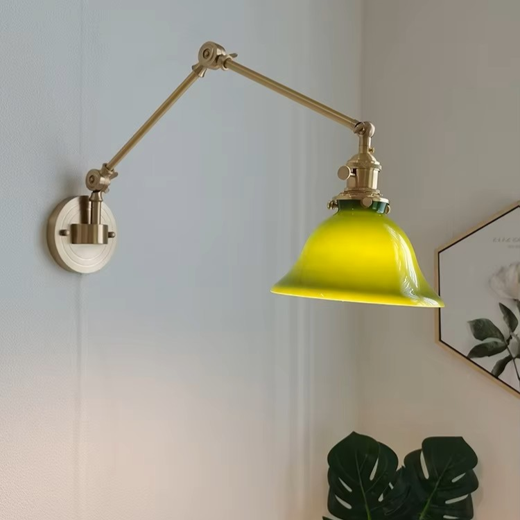 Adjustable wall sconce with a brass-colored metal arm and a vibrant green glass shade, mounted on a white wall in a styled room corner.