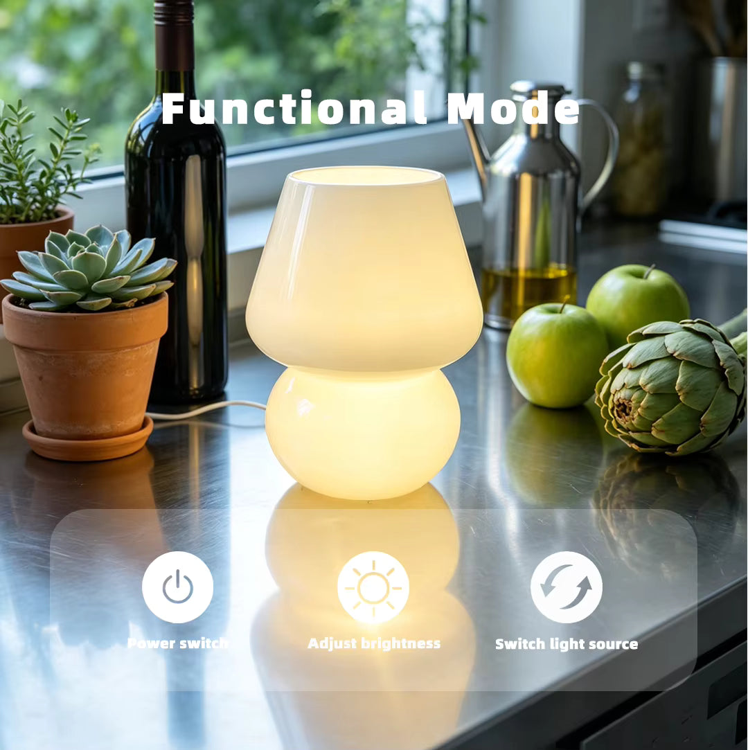 A glowing two-tiered table lamp sits on a stainless steel countertop in a kitchen setting, surrounded by a wine bottle, succulent, green apples, and an artichoke. White text overlays read 'Functional Mode' along with icons for power switch, brightness adjustment, and light source switching.