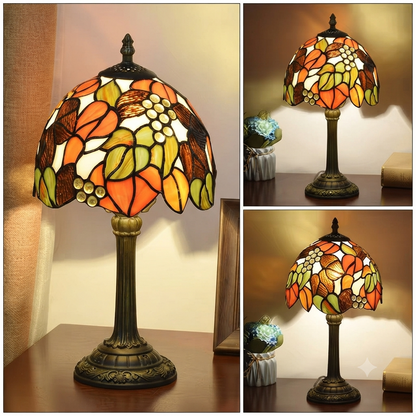 A stained glass table lamp with an ornate dark bronze base and a dome-shaped shade featuring a floral and grape design in orange, yellow, green, and brown, shown in a three-panel collage on a warm indoor background.