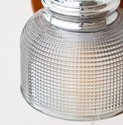 Close-up of a textured clear glass shade or lamp body with a shiny silver metal collar, showing warm light glowing through the ribbed transparent surface.