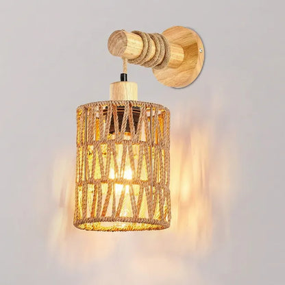 A rustic wall-mounted light fixture with a cylindrical woven rope shade, natural wood wall plate and arm, and a glowing warm bulb inside, shown against a light gray wall.