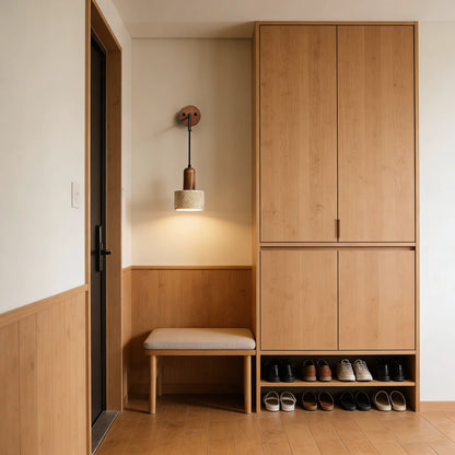 A modern minimalist entryway featuring a light oak wood entryway cabinet with a built-in bench, a wall-mounted pendant light, and an open shoe rack at the bottom. The space is styled with neutral beige and warm wood tones.