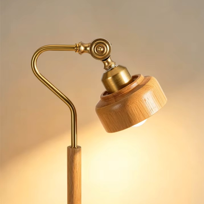 A modern adjustable floor lamp with a warm brass metal arm and a round light-wood shade, shown illuminated against a soft beige background.