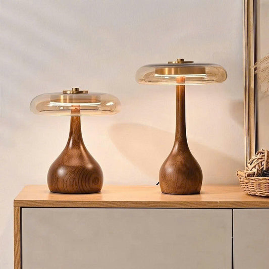 Two modern table lamps with curved wooden bases and translucent glass shades, shown lit on a light wood cabinet against a neutral wall.