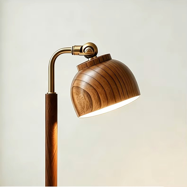 A modern floor lamp with a warm brown wood-grain shade and matching wooden pole, featuring a curved brass metal arm and adjustable head, shown lit against a soft off-white background.