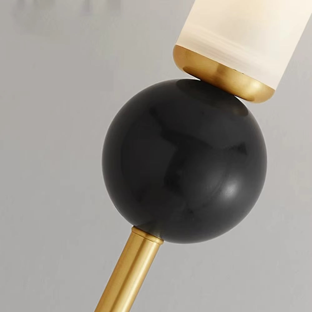 Close-up of a modern lamp with a glossy black spherical shade, a gold-finished metal stem and collar, and a frosted white cylindrical shade at the top, set against a plain light gray background.