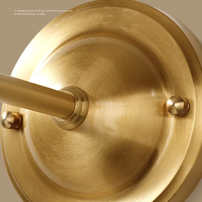 Close-up of a brushed brass or gold metal wall fixture base with a mounting rod and two visible screws on a warm beige background.