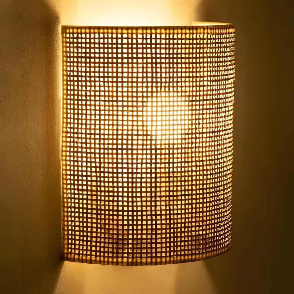 A cylindrical wall sconce with a warm glowing mesh shade, mounted on a textured beige wall.